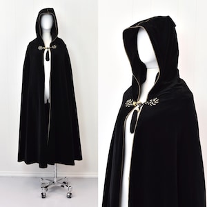 May include: A black velvet hooded cape with gold trim and decorative accents. The cape has a long, flowing design and a high collar.