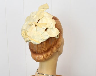 May include: A white vintage hat with a flower design. The hat is made of fabric and has a delicate, feminine look.