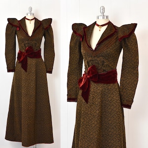 May include: A vintage-style brown dress with a repeating pattern, long sleeves, and a V-neckline. The dress features a burgundy velvet trim on the collar, cuffs, and a wide belt with a large bow. A matching burgundy choker necklace completes the look.