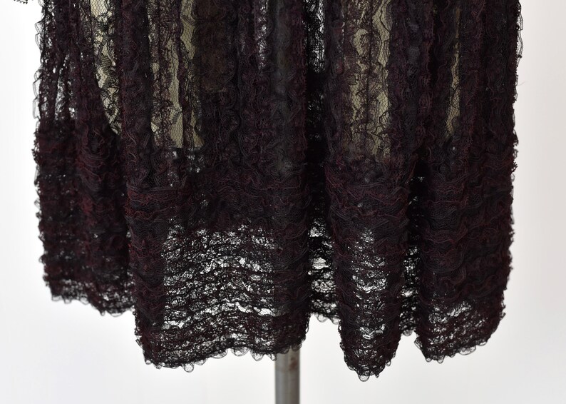 May include: Black lace fabric with a ruffled edge. The lace is delicate and has a vintage feel.