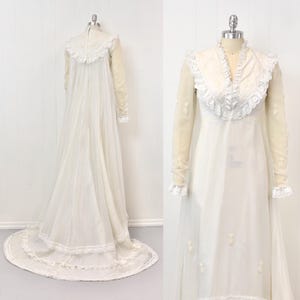 May include: A vintage ivory wedding dress with long sheer sleeves and a high neckline. The dress features delicate lace trim on the collar, cuffs, and hem, with floral embroidery on the bodice and sleeves. The dress has a long train.