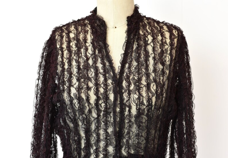 May include: A black lace top with a ruffled collar and long sleeves.