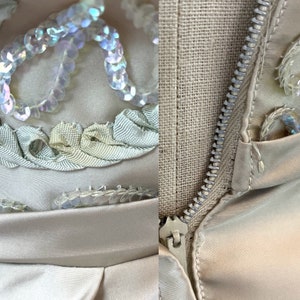 Op de afbeelding: Een close-up van een beige jurk met een rits aan de zijkant. De jurk is versierd met iriserende pailletten en lichtblauw lint.