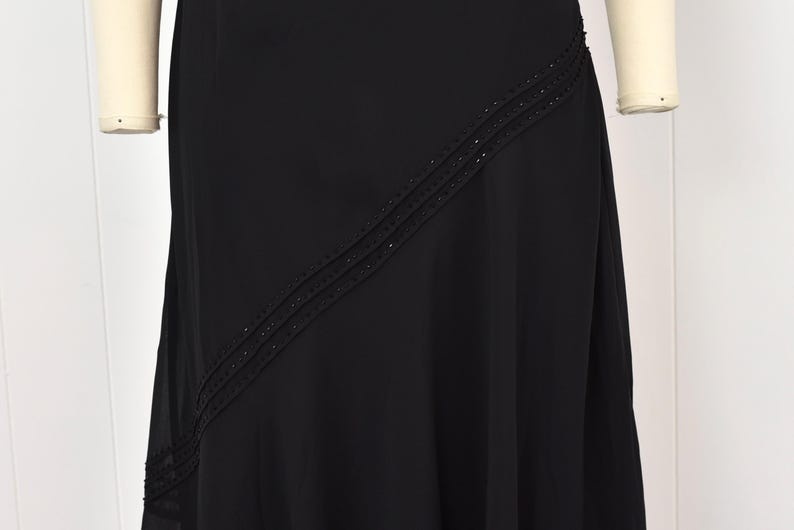 May include: A black formal dress with a flowing skirt. The dress has a diagonal beaded design across the front. The dress is displayed on a mannequin, showcasing its elegant drape and design. Suitable for special occasions.