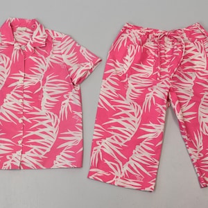May include: A pink and white tropical print pajama set with a short-sleeved button-up shirt and matching pants.