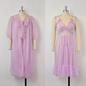 May include: Two vintage lilac-colored lingerie pieces displayed on mannequins. The first is a sheer robe with a large bow at the neckline and short sleeves. The second is a slip dress with spaghetti straps and a ruffled hem, both in a soft, flowing fabric.