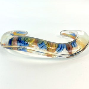 May include: A clear glass bangle bracelet with a swirl of blue, yellow, and brown colors inside.