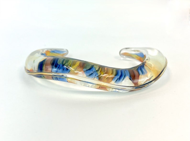 May include: A clear glass bangle bracelet with a swirl of blue, yellow, and brown colors inside.