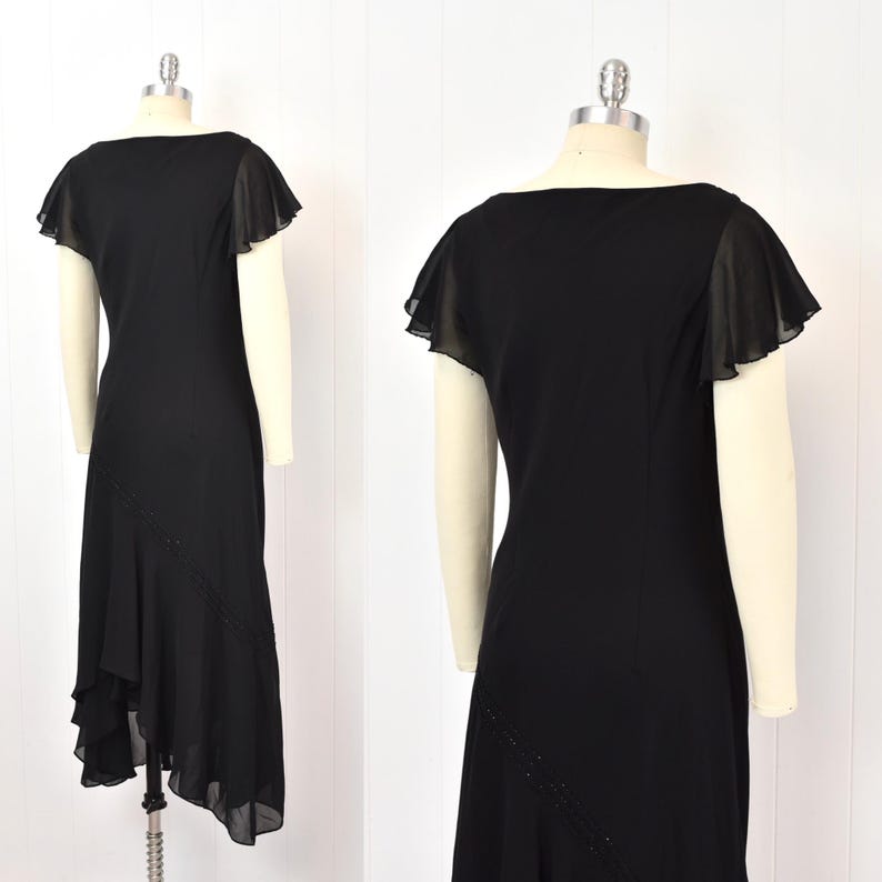 May include: A black dress with a square neckline and short, flutter sleeves. The dress has an asymmetrical hemline and a beaded detail. The dress is displayed on a mannequin.
