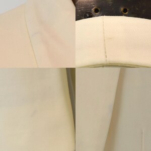 May include: Close-up of a cream-colored blazer. The fabric appears to be a smooth, woven material. The image shows details of the collar, lapel, and seams, highlighting the tailoring and construction of the garment. The blazer is a neutral color, suitable for various outfits.
