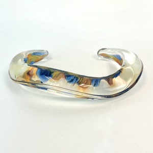 May include: A clear glass bangle with swirls of blue, yellow, and orange.