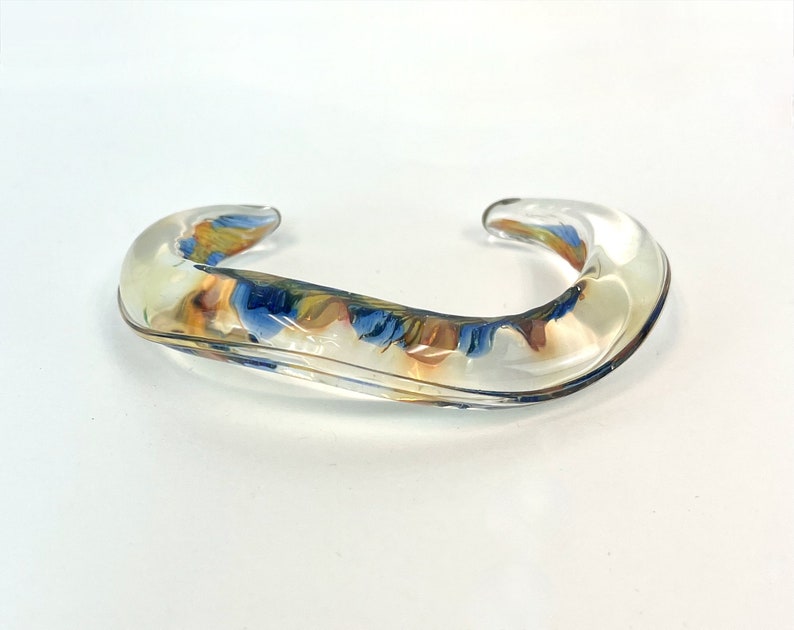 May include: A clear glass bangle with swirls of blue, yellow, and orange.