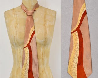 May include: A vintage tie in shades of peach, tan, and rust, displayed on a mannequin. The tie features an abstract design with curved lines and a textured pattern. The tie is knotted at the neck.