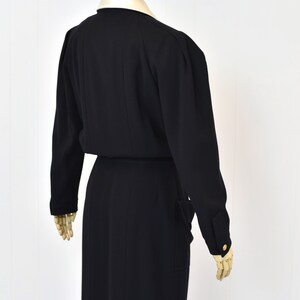 May include: A black long-sleeved dress with a collared neckline and a fitted silhouette. The dress has a belt at the waist and pockets on the sides.