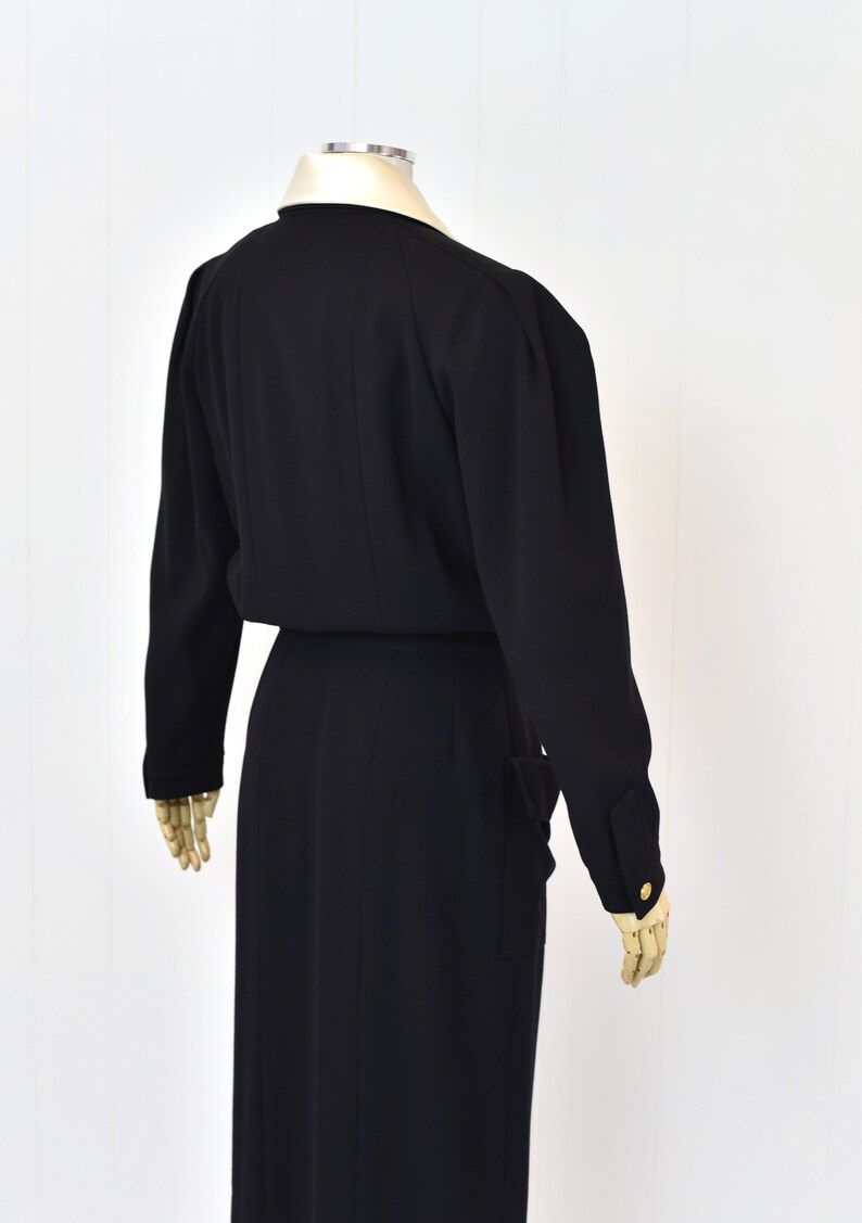 May include: A black long-sleeved dress with a collared neckline and a fitted silhouette. The dress has a belt at the waist and pockets on the sides.