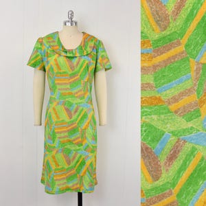 May include: A knee-length dress featuring a short-sleeved design and a wide, rounded collar. The fabric displays a vibrant, abstract geometric pattern composed of textured, overlapping shapes in shades of bright green, yellow, brown, and light blue.