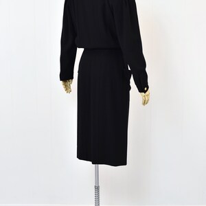 May include: A black dress with long sleeves and a fitted silhouette. The dress has a V-neckline and a belt at the waist. The dress is on a mannequin on a white background.