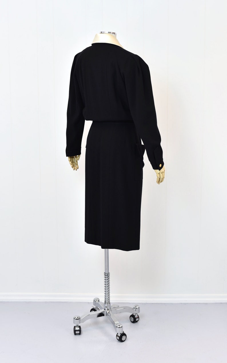 May include: A black dress with long sleeves and a fitted silhouette. The dress has a V-neckline and a belt at the waist. The dress is on a mannequin on a white background.