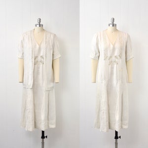 May include: A white linen dress with a crocheted design on the bodice. The dress has a v-neckline and short sleeves. It is a vintage style dress.