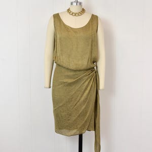 May include: Olive green vintage dress with a draped skirt and a matching gold-tone necklace. The dress is sleeveless and has a gathered waist detail. The dress is displayed on a mannequin.