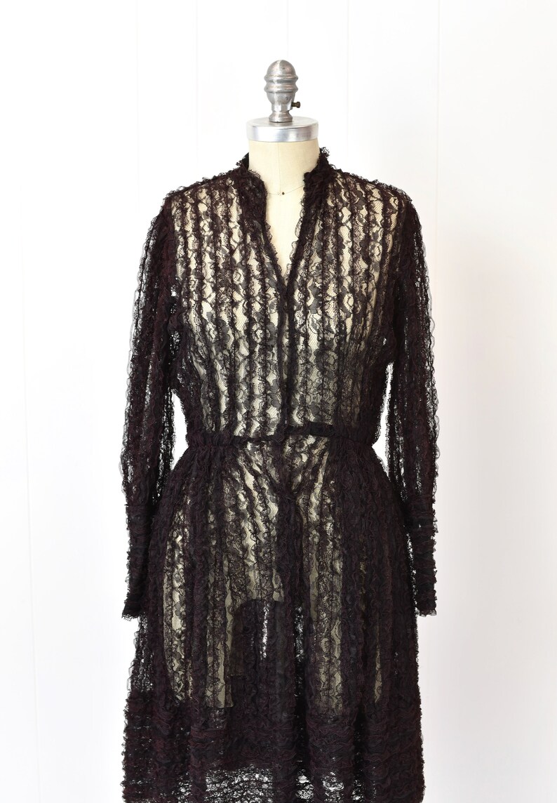 May include: A black lace dress with long sleeves and a ruffled hem. The dress is sheer and has a fitted bodice.