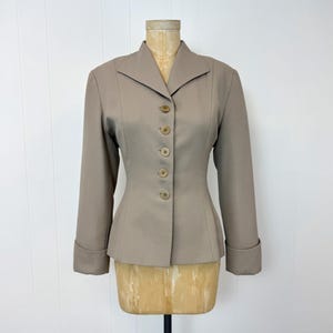 May include: A tan blazer with a tailored fit, displayed on a mannequin. The blazer features a notched collar, long sleeves with folded cuffs, and a row of five matching buttons down the front. The garment has a classic, structured design.
