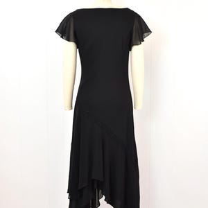 May include: A black dress with a square neckline and short, sheer flutter sleeves. The dress has an asymmetrical hemline and a diagonal beaded detail. The dress is displayed on a mannequin against a white background.