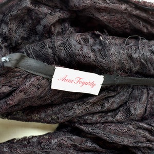 May include: Close-up of a black lace fabric with a white tag that reads "Anne Fogarty".