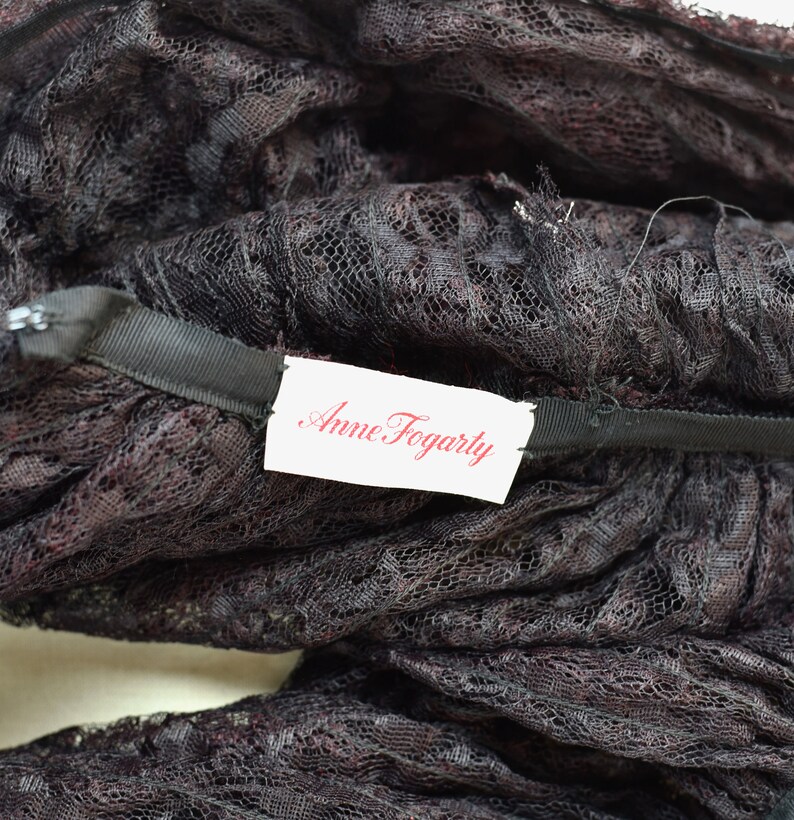 May include: Close-up of a black lace fabric with a white tag that reads "Anne Fogarty".