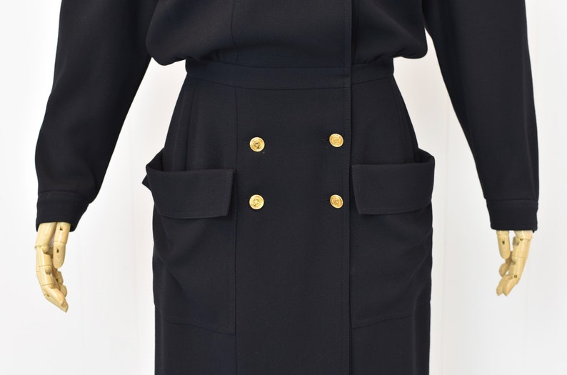 May include: A black long-sleeved dress with a double-breasted button closure and two large pockets on the front.