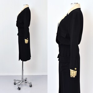 May include: A black long-sleeved dress with a white collar and gold buttons. The dress has a cinched waist and a knee-length skirt.