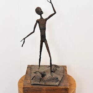 May include: A rusty metal sculpture of a person standing on a wooden base. The person is reaching up with one arm and has a distressed look on their face.