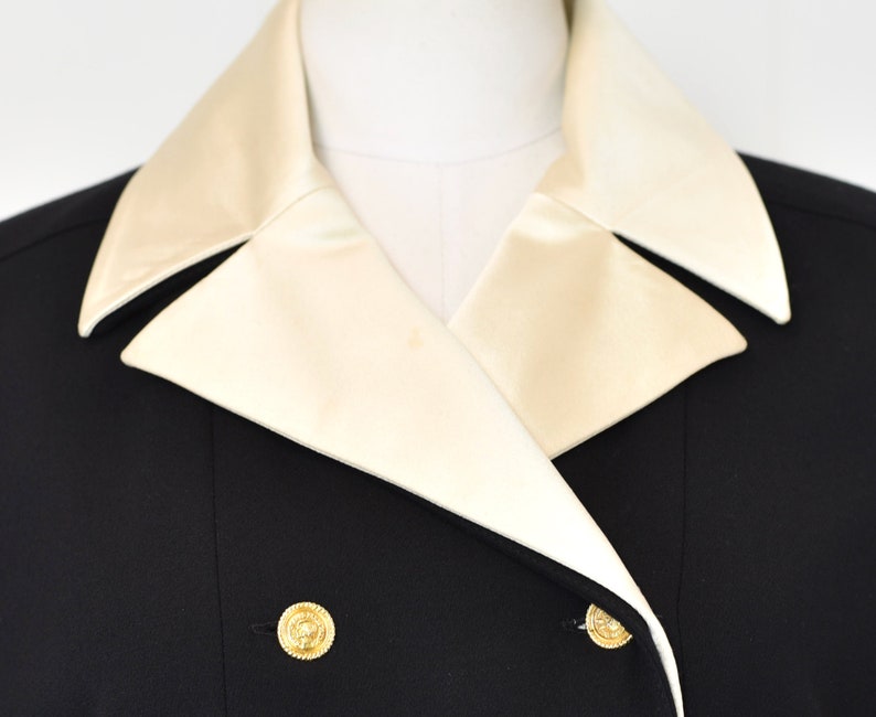 May include: A black double-breasted blazer with a white satin collar. The blazer has gold buttons.