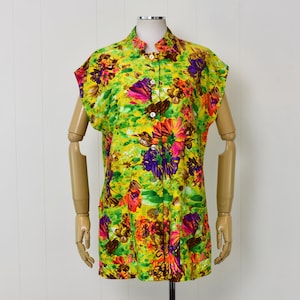 May include: A yellow sleeveless shirt with a floral print in shades of pink, purple, green, and brown. The shirt has a mandarin collar and a button-up front.