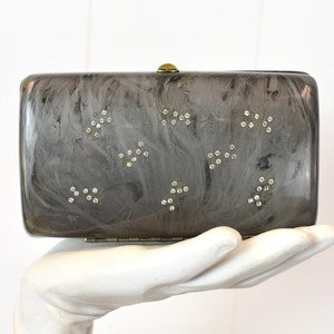 May include: A gray clutch purse with a marbled design and silver rhinestones. The purse has a gold clasp.