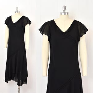 May include: A black dress with a V-neck and flutter sleeves. The dress has a diagonal beaded detail across the bodice and skirt. The hemline is asymmetrical, with a longer back. The dress is displayed on a mannequin.