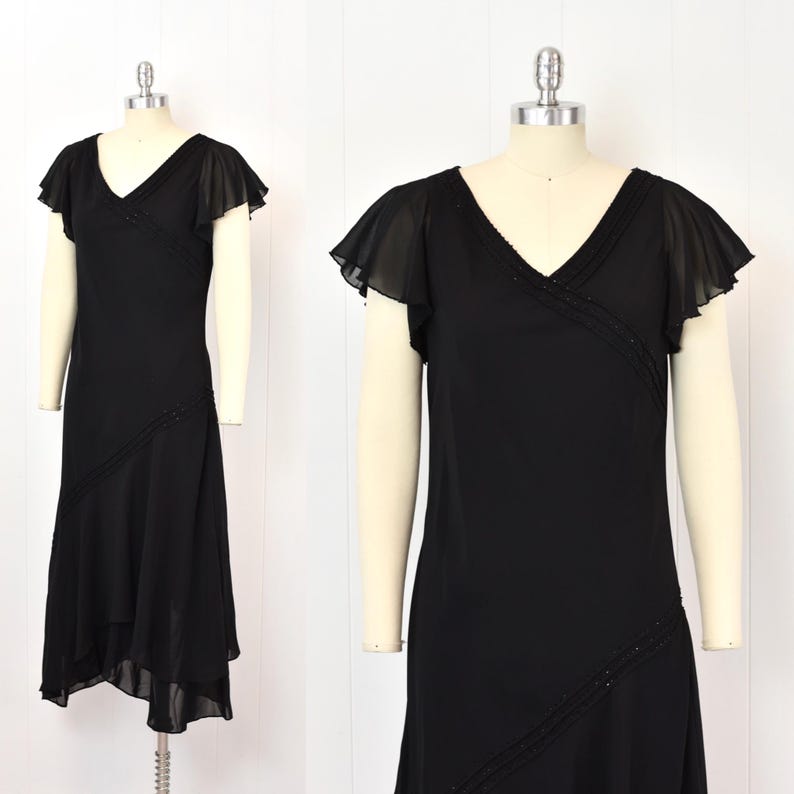 May include: A black dress with a V-neck and flutter sleeves. The dress has a diagonal beaded detail across the bodice and skirt. The hemline is asymmetrical, with a longer back. The dress is displayed on a mannequin.