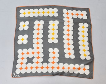 May include: A gray silk scarf with a geometric pattern of white circles with orange centers and yellow centers. The scarf has a black border and the text "Usna." in the lower left corner.