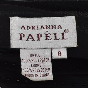 May include: A close-up of a black garment label featuring the brand name "Adrianna Papell". The label indicates the garment is size 8 and made of 100% polyester shell and lining. The label also states "Made in China."