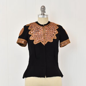 May include: A black short-sleeved blouse with a decorative neckline featuring a gold and brown mirrored design.