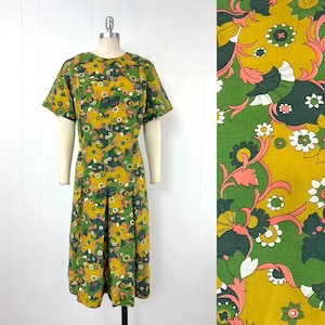 May include: A midi-length dress featuring a vibrant floral pattern in shades of mustard yellow, forest green, and soft pink. The garment has short sleeves, a round neckline, and a pleated skirt, displayed on a mannequin against a white background.
