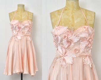 May include: A pink satin dress with a strapless bodice and a full skirt. The bodice is adorned with a large, intricate design of pink fabric flowers.