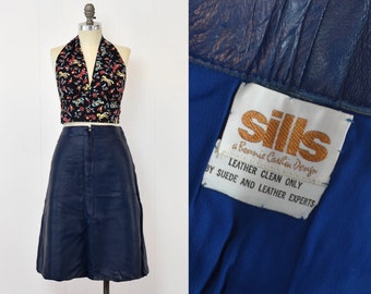 May include: A navy blue leather skirt with a zipper closure and a label that reads "Silks a Bonnie Caitlin Design Leather Clean Only By Suede and Leather Experts".