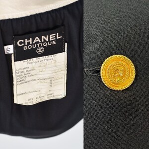 May include: Black blazer with a gold button featuring a profile of a woman. The label reads "CHANEL BOUTIQUE" and includes details about the fabric composition: "MADE IN FRANCE, Fabriqu&eacute; en France, Collection, STYLE/Modaie, SIZE/Tallle, COLOR/Coloris, FABRIC, COMPOSITION/Composition, 100% Soie, LINING/Doublure, DRY CLEAN ONLY, NETTOYER A SEC SEULEMENT".