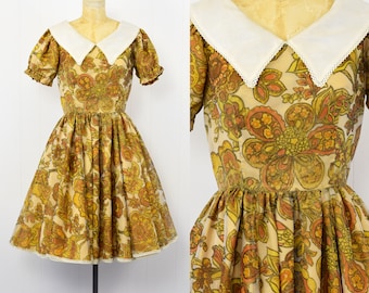 May include: A vintage 1960s dress with a large floral print in shades of orange, yellow, and brown. The dress has a white Peter Pan collar and short sleeves. The dress is made of a lightweight fabric and has a full skirt.