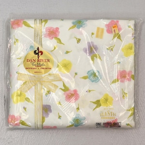 May include: A white fitted sheet with a floral pattern in shades of pink, yellow, blue, and green. The sheet is packaged in plastic and has a label that reads "Dan River Fine Muslin One Fitted Sheet Double Bottom".