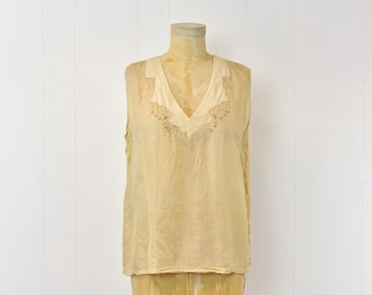 May include: A sleeveless, cream-colored blouse with a delicate floral embroidery design around the neckline.