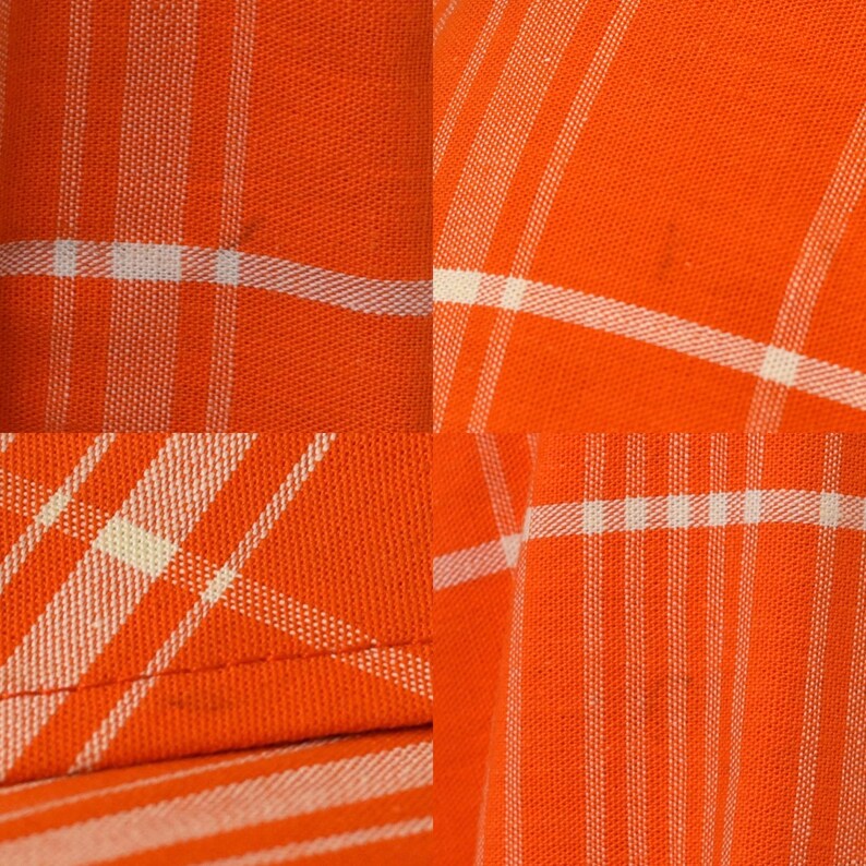 May include: Close-up of orange fabric with a white plaid pattern. The fabric has a woven texture, with the white lines intersecting to create a grid-like design. The orange color is vibrant and the white lines are crisp.