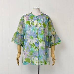 May include: A vintage floral print jacket with a round collar and button-up front. The jacket features a sheer fabric with a pattern of large blue, white, and green flowers. The sleeves have a ruffled bell shape, and the jacket is displayed on a mannequin.