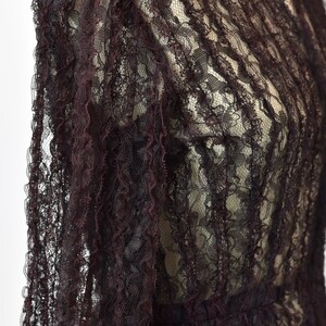 May include: A close-up of a dark burgundy lace fabric with a delicate floral pattern. The fabric is sheer and has a slightly ruffled texture.